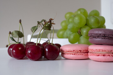 Appetizing mix of macarons and cherries with blurred green grapes in background. Light background.
