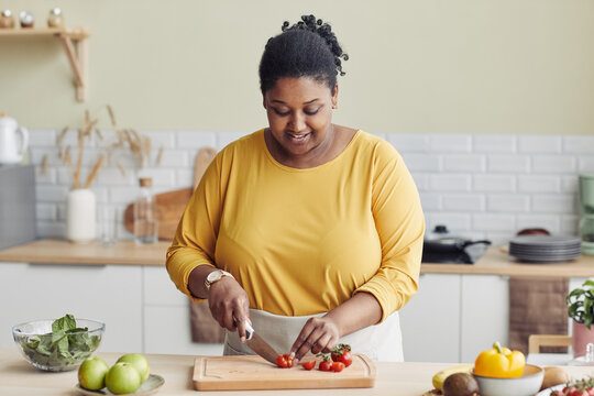 Waist up portrait of smiling black woman cooking healthy meal in kitchen and cutting vegetables, copy space