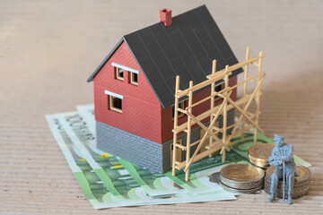 Miniature old man on Euro coins and blurred residential house model on background, house construction costs. Concept - dream of your own house in old age.