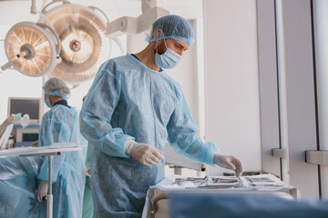 Professional doctor surgeon takes scalpel before surgery in operation room at the hospital - obrazy, fototapety, plakaty