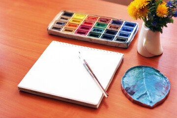 Sheet of paper and watercolor on the table. Paint accessories, watercolor and blank book on wooden table. (work place mock up, copy space, Isolated, white copy space,  Blank Copy Space