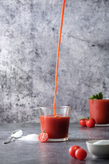 tomato juice, pour tomato juice into a glass, splashes of tomato juice, on a gray background, space for text, cherry tomatoes and salt 