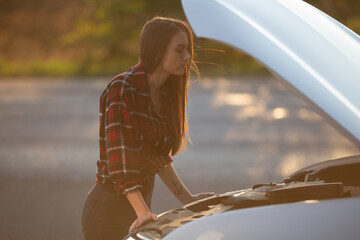 Car breakdown on road. Young desperate woman desperately trying to fix engine near broken car on road. Help needed. Car service.