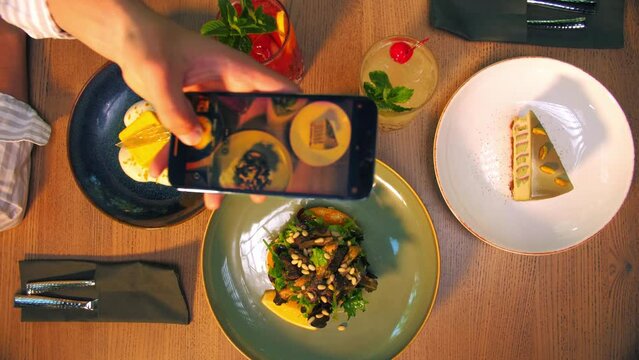 Men's hands photographing food with a smartphone in a restaurant.There are cocktail salads and two desserts on the table
