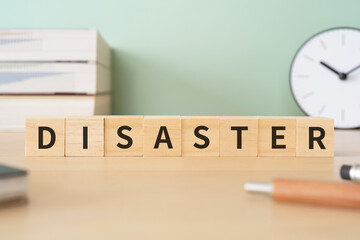災害・災難のイメージ｜「DISASTER」と書かれたブロックが置かれたデスク
