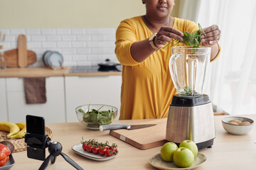 Cropped shot of black woman putting spinach in blender while making healthy smoothie at home, copy...