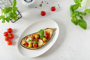Italian traditional dish with eggplant, tomatoes, olives, mozzarella and basil. Baked aubergine stuffed with vegetables on a white plate. Vegan menu recipe. Top view, copy space