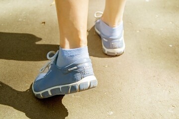 Close-up of women's legs in sports sneakers walking on an asphalt path on a sunny day. Walking with varicose veins. Tinting.