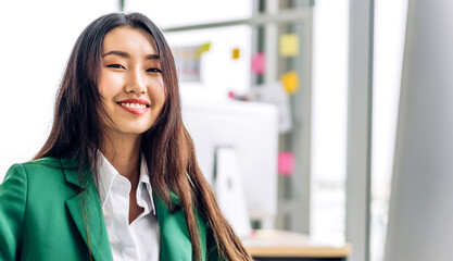 Beautiful happy confident asian businesswoman smart looking at camara while sitting on office workplace desk.Young creative coworkers business people working and planning