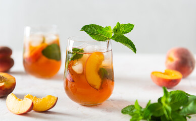 Homemade iced lemonade with ripe peaches and fresh mint. Fresh peach ice tea in glasses on a white...