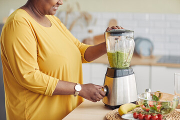 Side view closeup of black woman using blender while making healthy smoothie at home kitchen, copy...