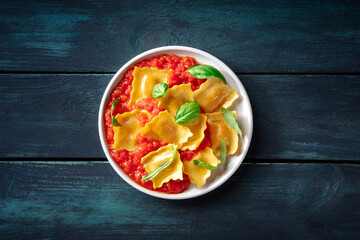 Ravioli with tomato sauce and fresh basil leaves on a plate, overhead flat lay shot on a dark wooden background