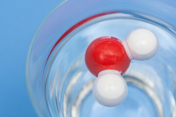 Chemical model of water molecule in plastic floating in a glass with water and blue background 