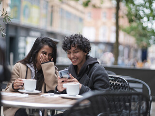 Smiling female couple using phone in sidewalk cafe