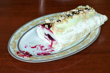 partially eaten homemade meringue roll with raspberry jam and pine nuts on a plate.
