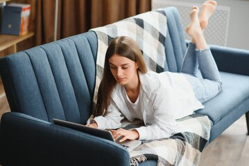 Obraz premium Freelancer working on laptop at home laying on comfortable beige sofa.