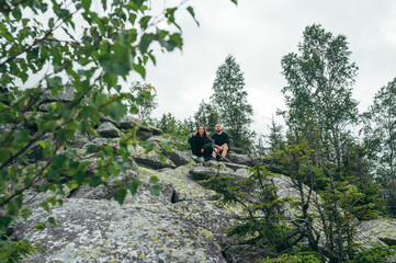 Obraz premium Two hikers man and woman sitting on a rock during a hike and resting, looking at the camera and smiling.