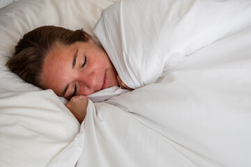 Fototapeta na wymiar Mujer durmiendo plácidamente en cama con sábanas y frazadas blancas