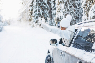 Teenager girl looking out of car window traveling in winter snowy forest. Road trip adventure and local travel concept. Happy child enjoying car ride. Christmas winter holidays and New year vacation
