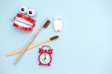 Time to brush your teeth. Toothbrushes and alarm clock on blue background, copy space