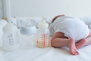 Baby's little butt with bend up legs and three bottles for milk on white blanket. Newborn - happiness for family. Concept of choice milk formula and food for kid. Back view