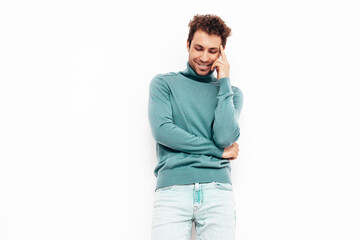 Portrait of handsome confident  model. Sexy stylish man dressed in blue sweater and jeans. Fashion hipster male with curly hairstyle posing near white wall in studio. Isolated