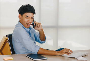 Young Asian businessman talking on the phone while sitting at his desk.