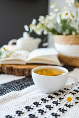 Fototapeta na wymiar Cup of chamomile tea, open book, wicker basket with flowers, atmospheric photo