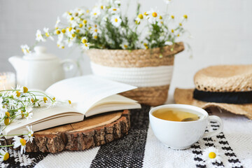 Open book, herbal chamomile tea cup on wooden table, reading and morning relax concept