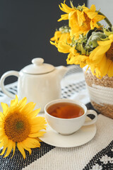 Obraz na płótnie Canvas A cup of tea and a teapot with a candle on a table with sunflowers, tea time, aesthetics