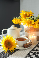 Obraz na płótnie Canvas A cup of tea and a teapot with a candle on a table with sunflowers, tea time, aesthetics