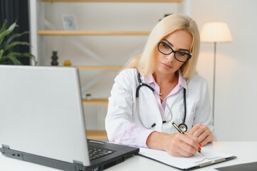 Shot of a female doctor working while sitting at desk in front of laptop