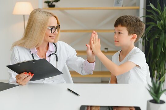 Smiling Woman Doctor Or Nurse Give High Five To Excited Little Boy Patient At Consultation In Clinic, Happy Small Child Have Fun Greet With Female Pediatrician In Hospital, Healthcare Concept