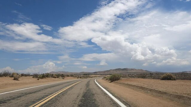 Point of view driving on a Mojave Desert highway in Apple Valley, California with blue sky and puffy clouds