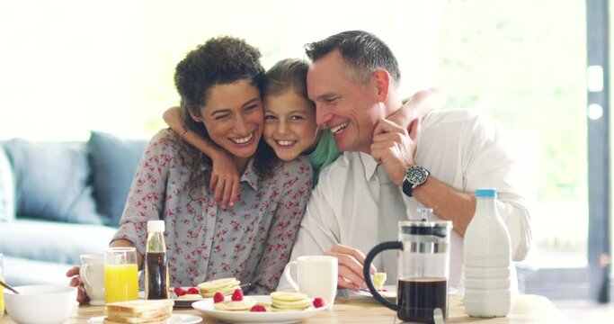 Happy family eating breakfast and enjoying the morning at home. Foster mother and father with their adopted daughter bonding, sharing and spending time together in their living room or kitchen