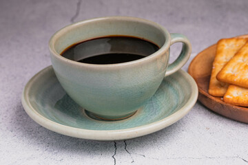 Hot black coffee in a green coffee cup with crackers.
