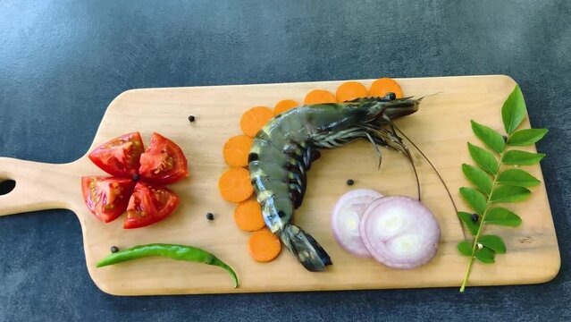 Fresh Giant Tiger Prawn decorated with herbs and vegetables on a wooden pad.