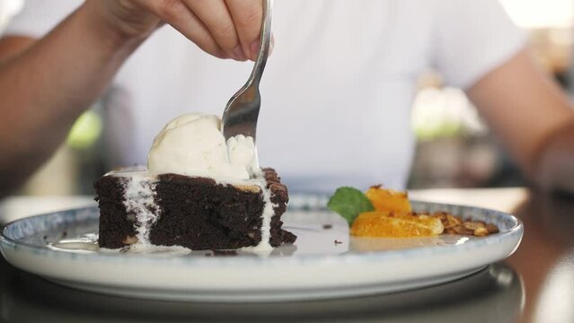 Person taking bite of chocolate cake with ice cream close up. Sweet breakfast.