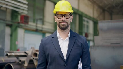 Engineer businessman with protective helmet in factory, checking blueprints and looking at camera.