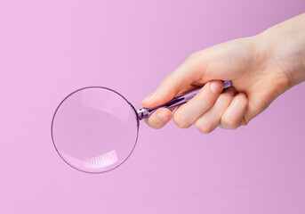 Magnifying glass lens in hand close up over pink background.