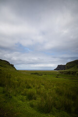 Fototapeta na wymiar Wide angle views of Talisker Bay, Isle of Skye, Scotland, with its rocky beach, black stones, green fields, and a waterfall at the end of beach. Scattered clouds on blue sky, summer scottish weather.