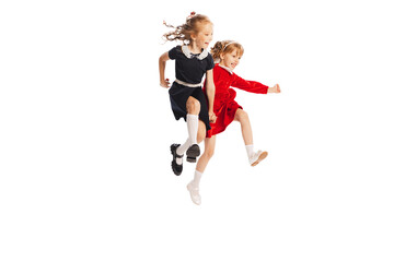 Fototapeta na wymiar Portrait of two cheerful girls, children jumping over puddle, running isolated over white studio background. Playful