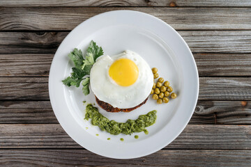 Scrambled eggs with meat on a plate, garnished with green peas and pesto sauce.