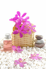 Spa setting with pink orchid in basket and oil bottle ,stacked stone on pile white stones background