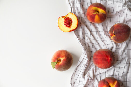 Ripe peaches whole and halved on white checkered fabric on white background