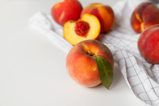 Ripe peaches whole and halved on white checkered fabric on white background