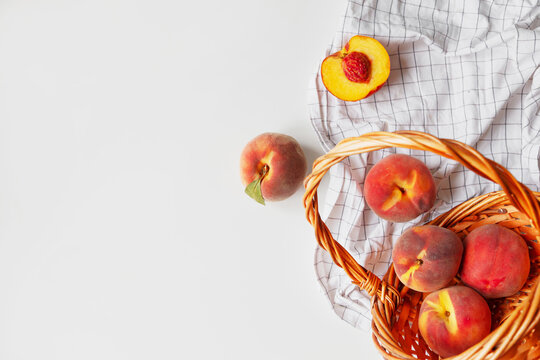 Ripe peaches in basket on white checkered fabric on white background