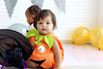 Adorable baby girl kid dressing up in orange fancy Halloween pumpkin costume, cheerful little cute child go to party, playing trick or treat, Happy Halloween celebration.