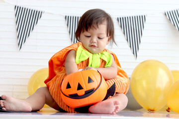Adorable baby girl kid dressing up in orange fancy Halloween pumpkin costume, cheerful little cute child go to party, playing trick or treat, Happy Halloween celebration.