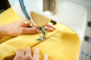 Obraz na płótnie Canvas Seamstress female hands holding and stitching yellow textile fabric on modern sewing machine at workplace. Sewing process, upholstery, clothes, repair, DIY. Handmade, hobby, small business concept